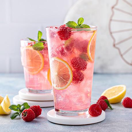 A glass of handmade pink lemonade with raspberries and lemon slices
