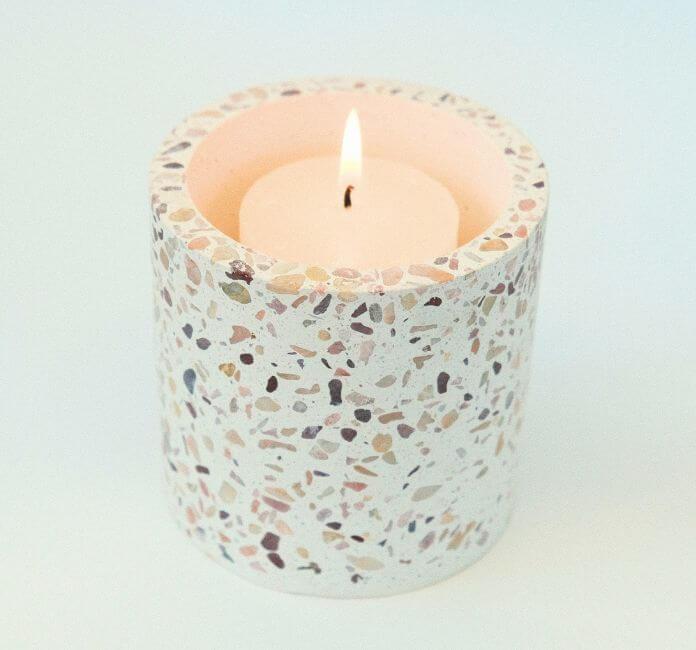 A Pink Terrazzo Jar, with a candle burning, on a white background.