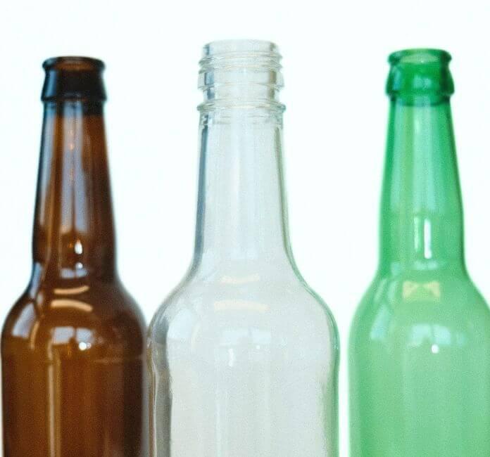 Three glass cider bottles, amber, clear and green, on a white background.