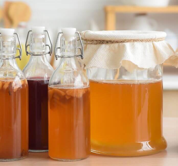 One glass jar, and three glass bottles with kombucha in.