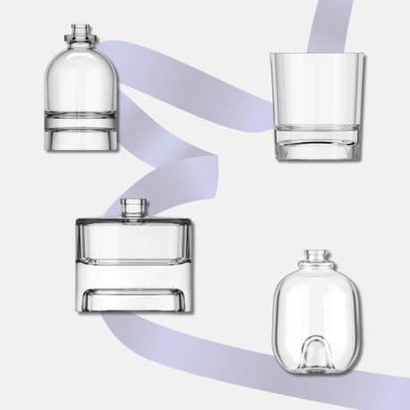 Four glass candle jars and glass diffusers on a grey background, with a purple ribbon behind.