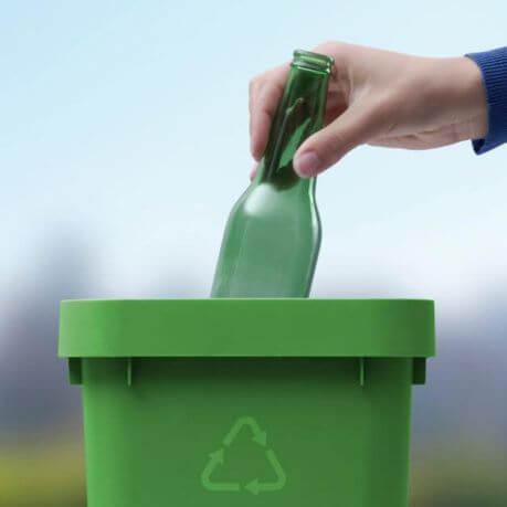 Person recycling a green glass bottle.