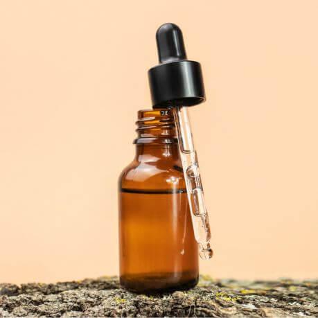 An amber glass dropper bottle, on a pink background.